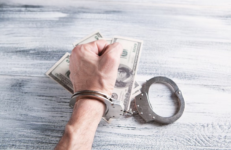 Рука в наручниках, сжимающая пачки долларов — символ коррупции и наказания за финансовые преступления - антикоррупционная культура