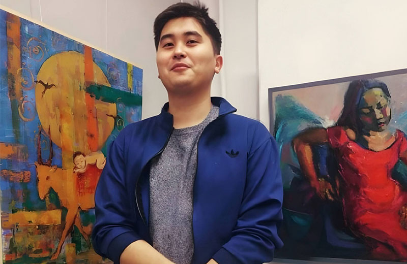 Ануар Қошқарбаев: қазақ хоррорына жаңа тыныс Ануар Кошкарбаев на фоне картин с выставки. Ануар Қошқарбаев қазақ хоррорына жаңа тыныс сыйлады